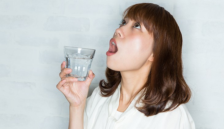 Eine Frau haelt ein Glas Wasser in Ihrer rechten Hand und gurgelt
