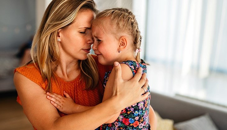 Eine Mutter haelt ihre weinende Tochter im Arm