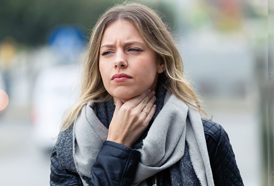 Eine Frau mit Schal fässt sich vor Schmerzen an den Hals