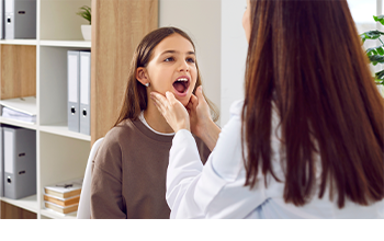 Eine Ärztin untersucht den Rachen einer Patientin und tastet die Mandeln ab