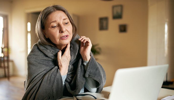 Eine Frau sitzt mit Halsschmerzen vor Ihrem Laptop