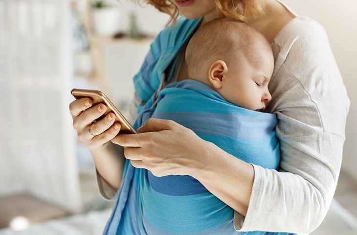 Ein Kind schlaeft im Arm der Mutter in einem Tuch eingewickelt