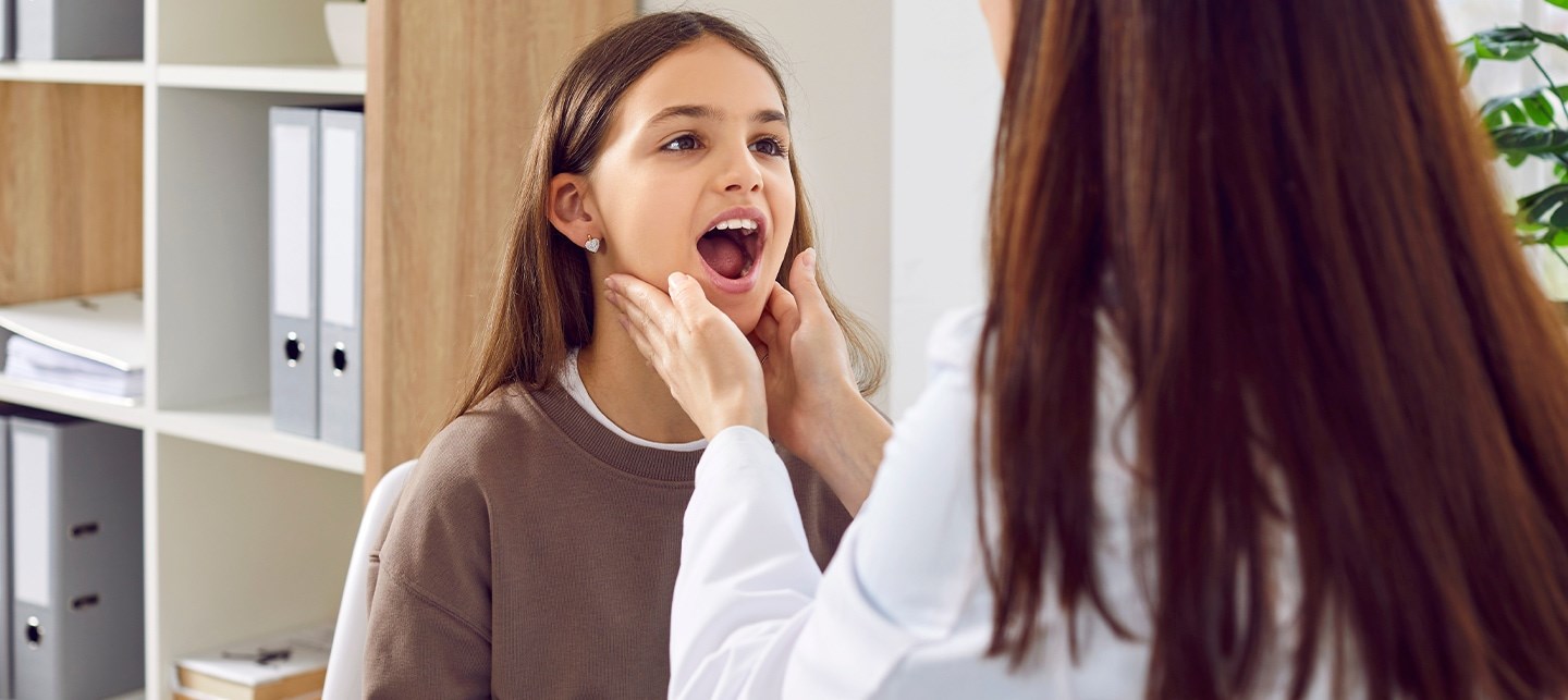 Eine Ärztin untersucht den Rachen einer Patientin und tastet die Mandeln ab