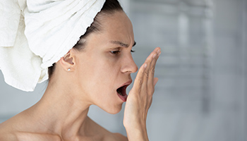 Halbseitliche Kopf- und Schulteransicht einer Frau mit Handtuchturban, die mit kritischem Blick ihre eigene Hand anhaucht.