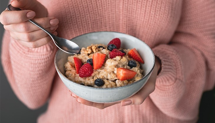 Person hält eine Schüssel Porridge mit Beeren und Walnüssen in den Händen.