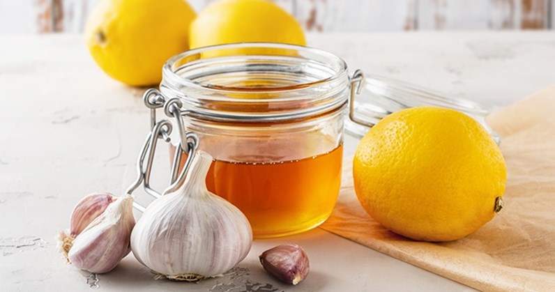 Honigglas umgeben von Knoblauch und Zitronen