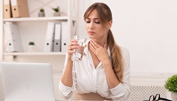 Eine Frau mit Halsschmerzen trinkt Wasser