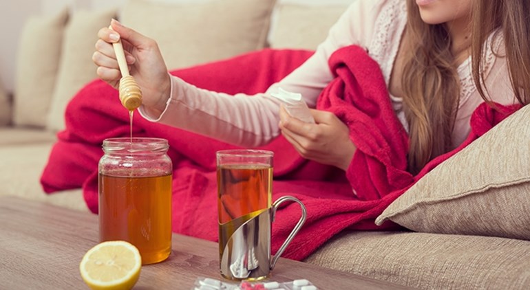 Eine Frau sueßt ihren Tee mit Honig waehrend sie auf dem Sofa liegt
