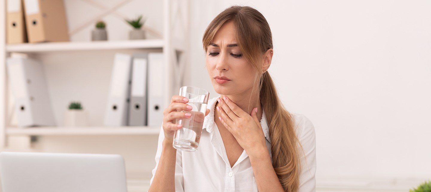 Eine Frau mit Halsschmerzen trinkt Wasser