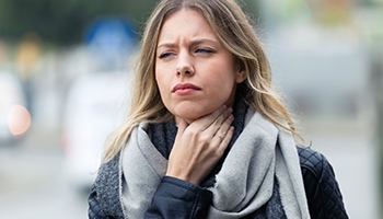 Eine blonde Frau mit langem Haar fasst sich an ihren Hals