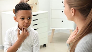 Ein Junge macht einer Logopädin Stimmenübungen und fässt sich dabei an den Hals