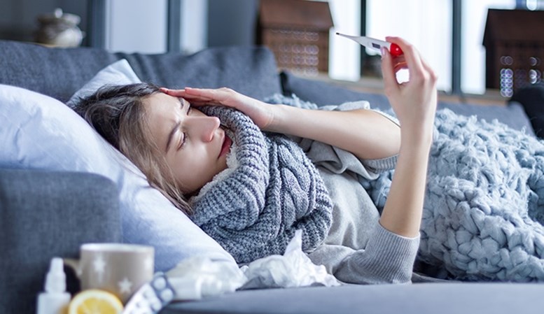 Eine Frau misst ihr Fieber liegend auf dem Sofa