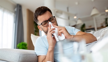 Ein Mann auf einem Sofa putzt sich die Nase