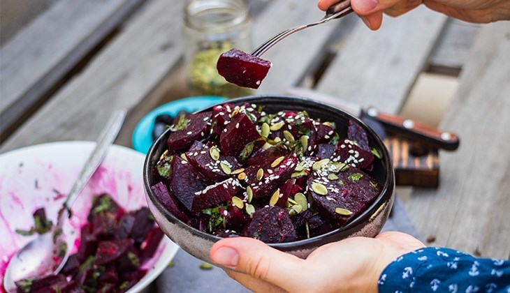 Person hält eine Schüssel mit Rote-Bete-Salat, garniert mit Kürbiskernen und Sesam.