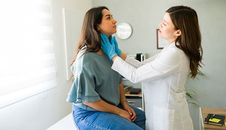 Ärztin tastet den Hals einer jungen Frau in einem hellen Praxisraum ab