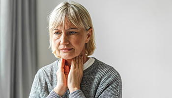  Eine Frau hält sich mit beiden Händen den schmerzenden Hals