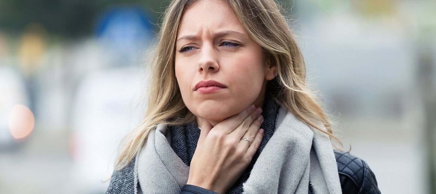 Eine blonde Frau mit langem Haar fasst sich an ihren Hals